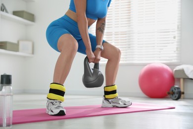 Photo of Beautiful woman with ankle weights and kettlebell training indoors