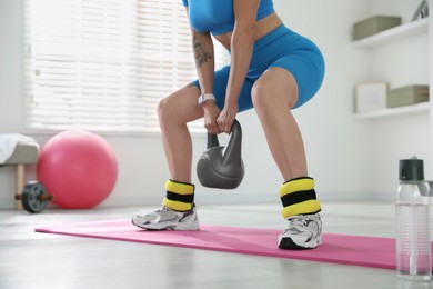 Photo of Beautiful woman with ankle weights and kettlebell training indoors