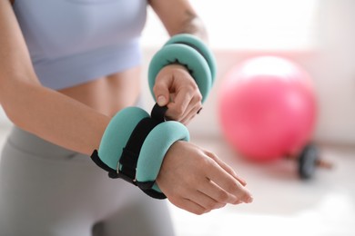 Woman putting ankle weight on her arm indoors, closeup