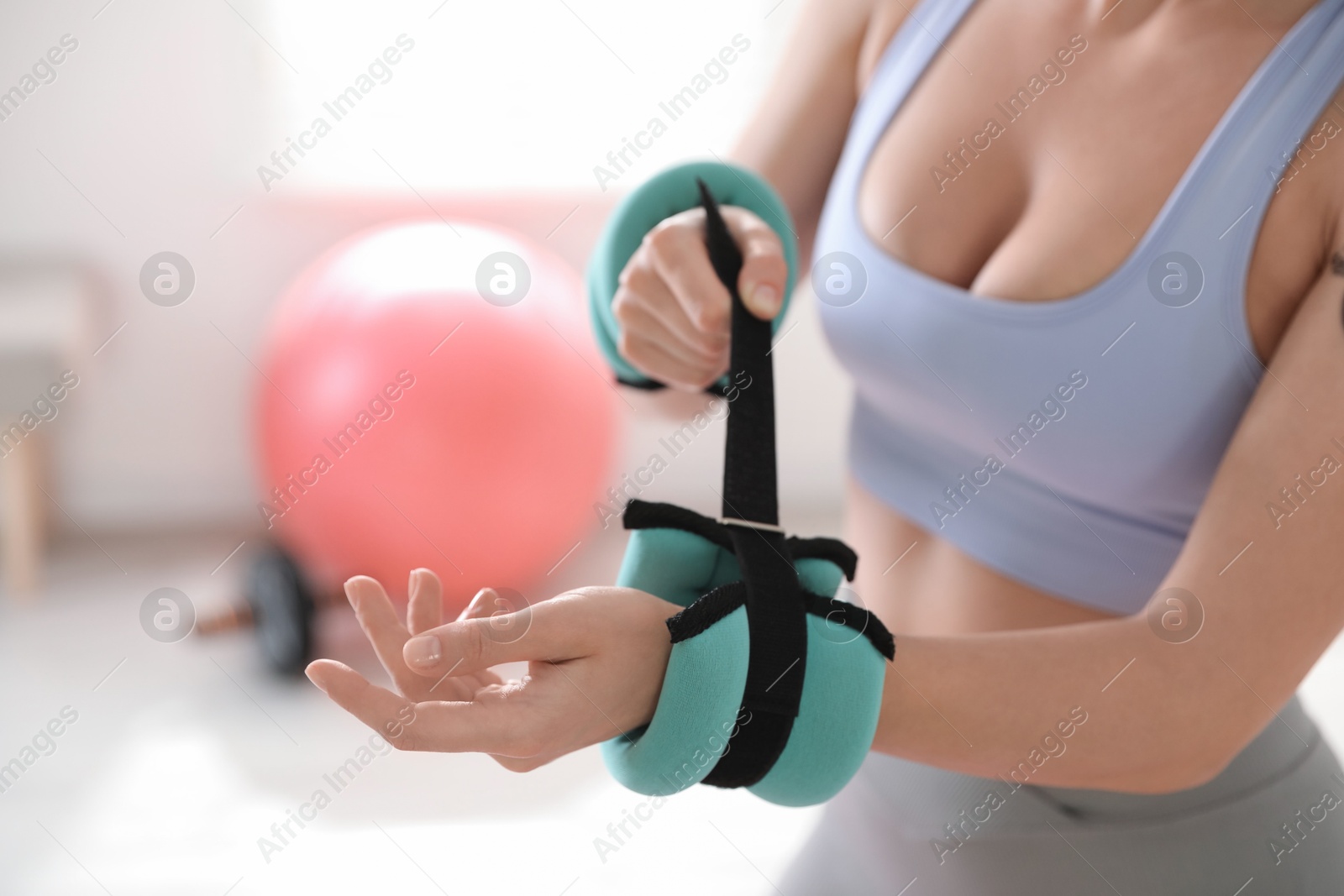 Photo of Woman putting ankle weight on her arm indoors, closeup