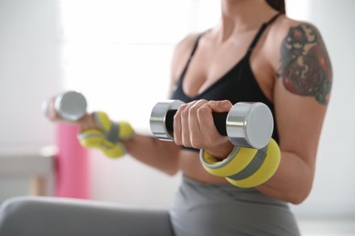 Photo of Woman with ankle weights and dumbbells training indoors, closeup