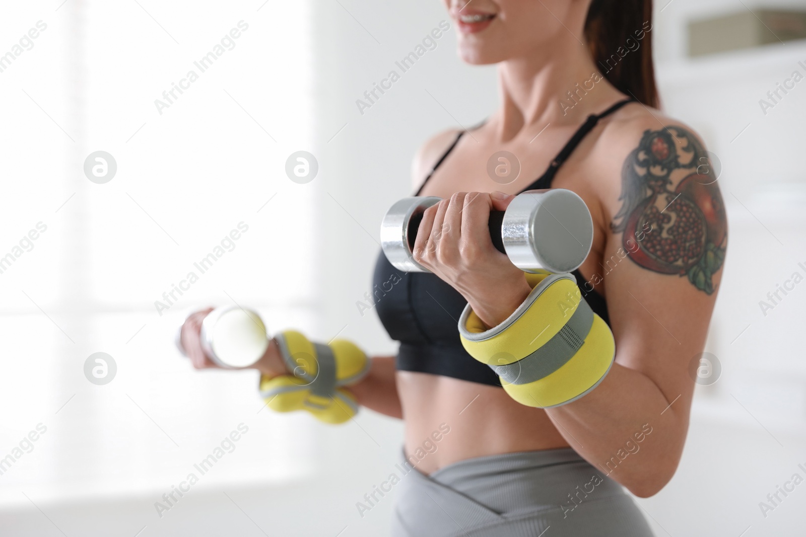 Photo of Woman with ankle weights and dumbbells training indoors, closeup