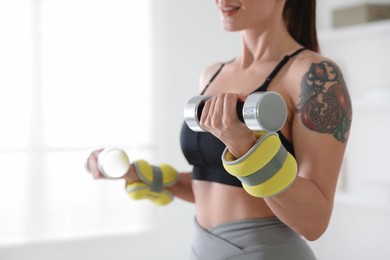 Photo of Woman with ankle weights and dumbbells training indoors, closeup
