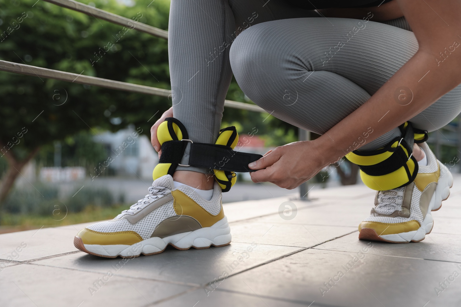 Photo of Woman putting on ankle weights outdoors, closeup