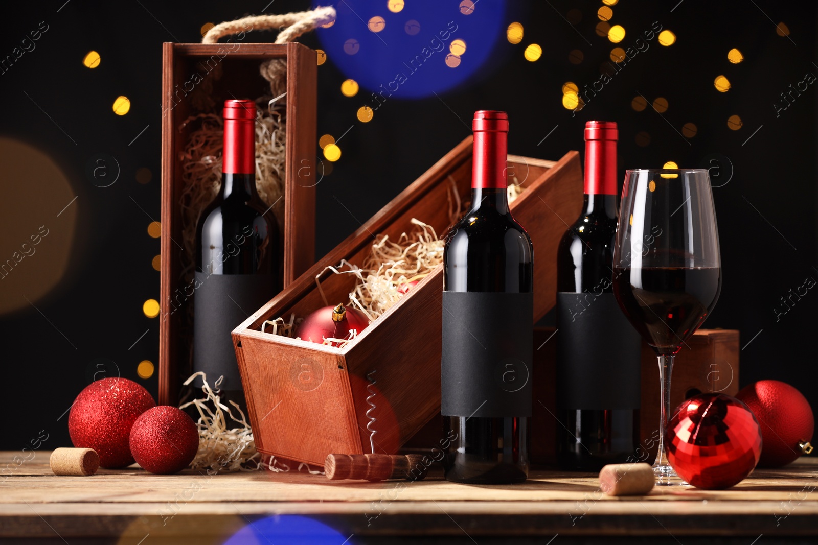 Photo of Bottles of wine, glass, wooden boxes, corks and red Christmas balls on table