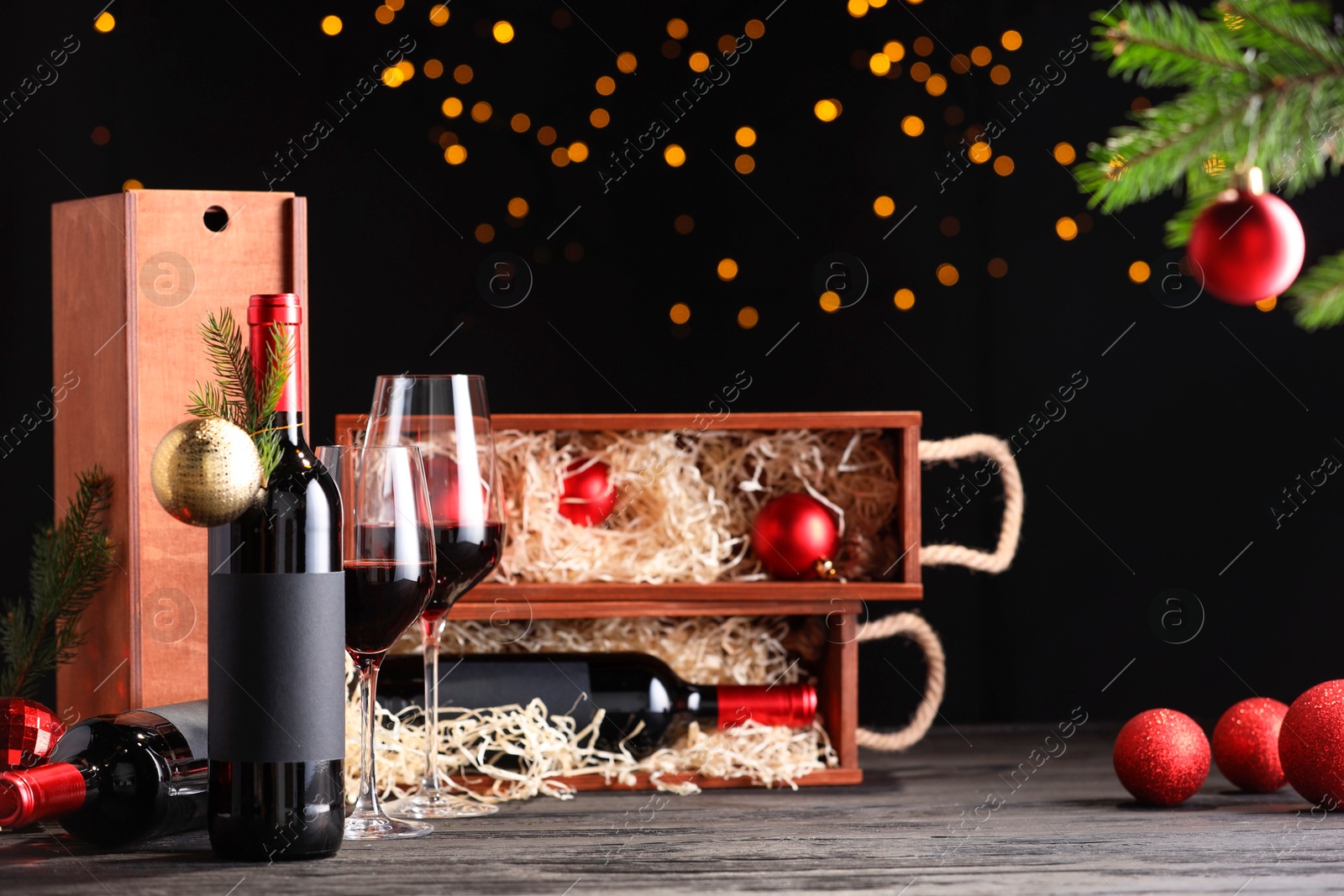 Photo of Bottles of wine, glasses, wooden boxes, fir twigs and Christmas balls on table