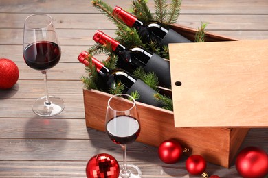 Photo of Wooden crate with bottles of wine, glasses, fir twigs and red Christmas balls on table