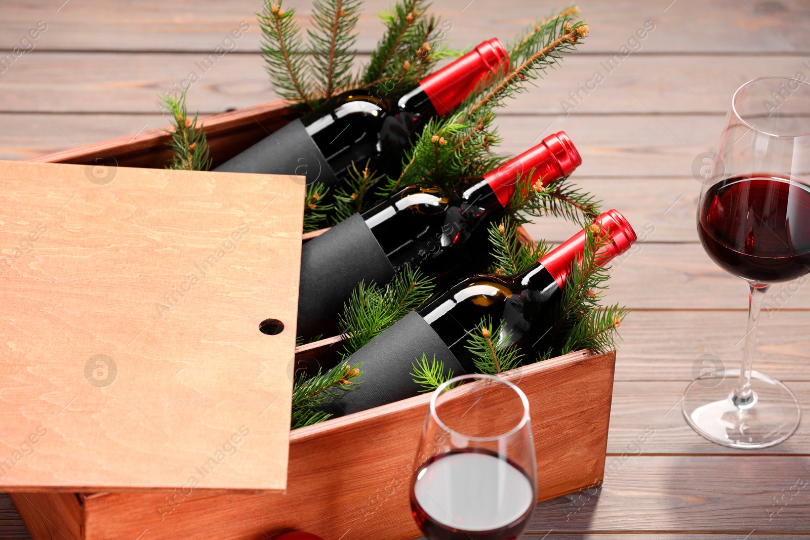 Photo of Wooden crate with bottles of wine, glasses, fir twigs and red Christmas balls on table