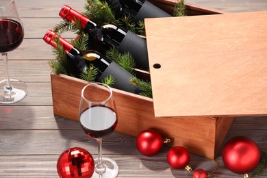 Photo of Wooden crate with bottles of wine, glasses, fir twigs and red Christmas balls on table