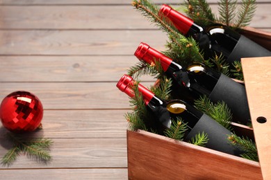 Photo of Wooden crate with bottles of wine, fir twigs and red Christmas ball on table, space for text