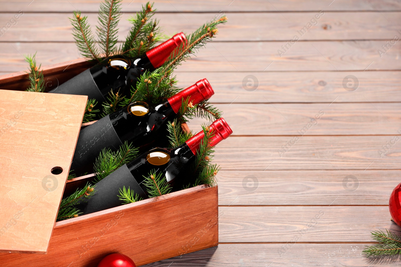 Photo of Wooden crate with bottles of wine, fir twigs and red Christmas balls on table, space for text