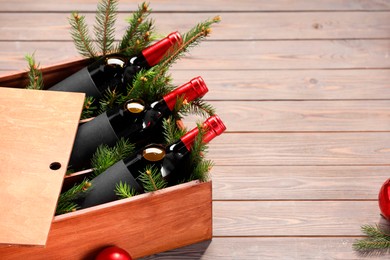 Photo of Wooden crate with bottles of wine, fir twigs and red Christmas balls on table, space for text