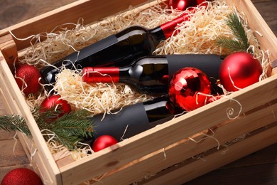 Photo of Wooden crate with bottles of wine, fir twigs and red Christmas balls on table