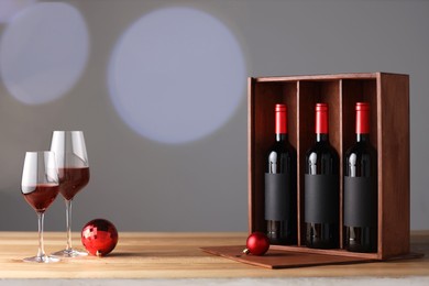 Photo of Wooden gift box with bottles of wine, glasses and red Christmas balls on table, space for text