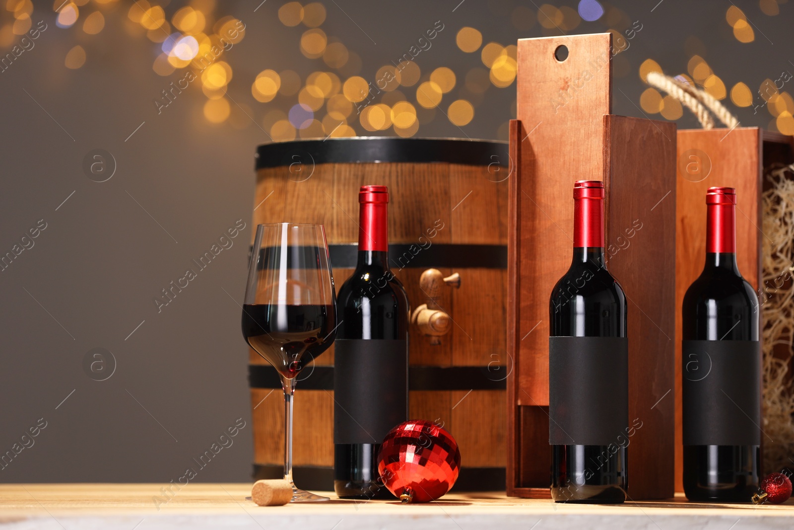 Photo of Bottles of wine, glass, wooden gift boxes, barrel corks and red Christmas balls on table, space for text