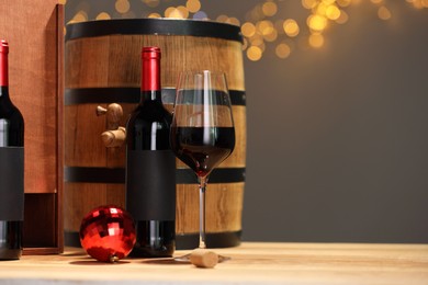 Photo of Bottles of wine, glass, wooden gift box, barrel cork and red Christmas balls on table, space for text