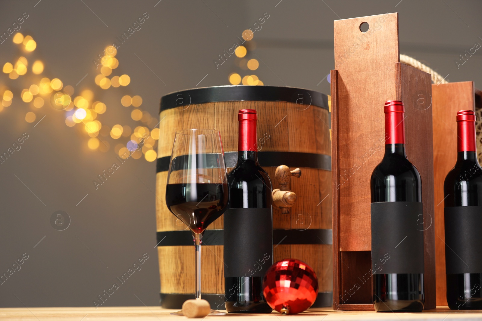 Photo of Bottles of wine, glass, wooden gift box, barrel cork and red Christmas balls on table, space for text