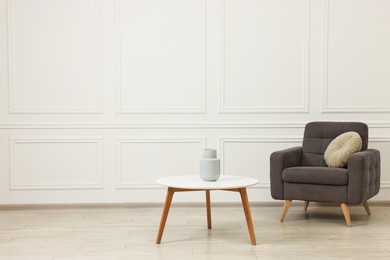 Photo of Soft armchair, coffee table and vase in stylish room. Space for text