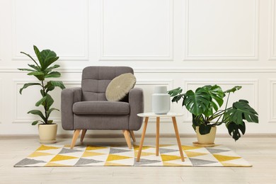 Soft armchair, coffee table and houseplants in stylish room