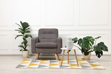 Soft armchair, coffee table and houseplants in stylish room