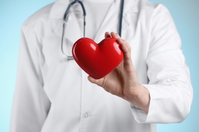 Photo of Doctor with red heart on light blue background, selective focus