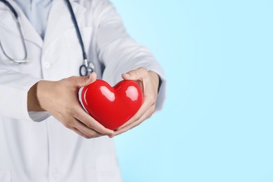 Photo of Doctor with red heart on light blue background, closeup. Space for text