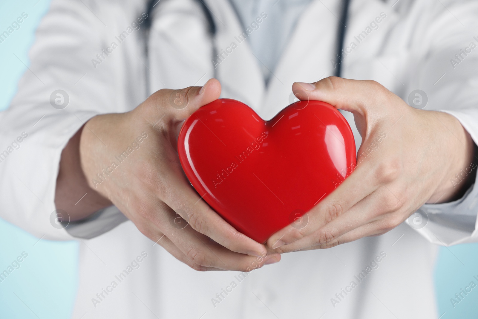 Photo of Doctor with red heart on light blue background, selective focus