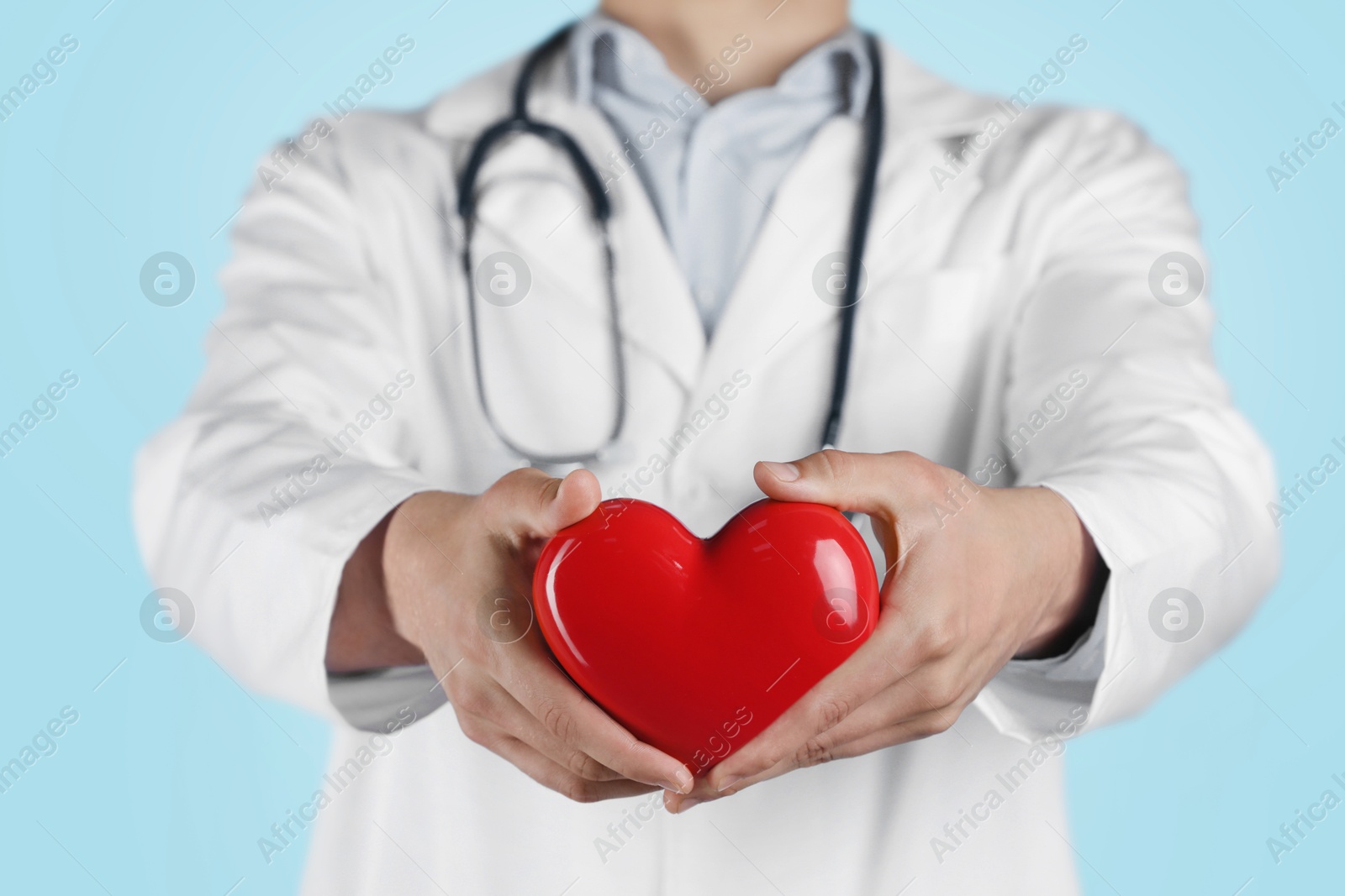 Photo of Doctor with red heart on light blue background, selective focus