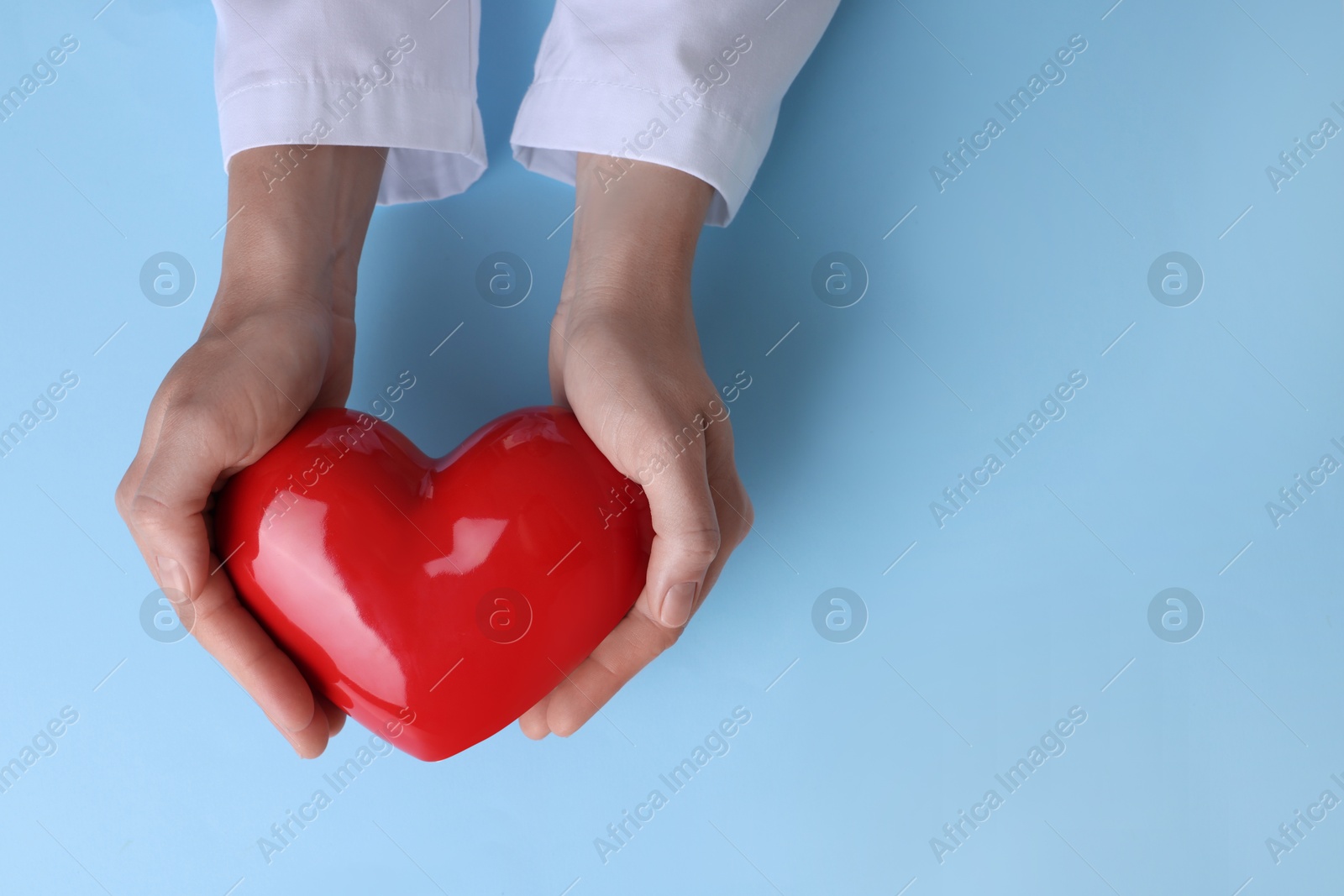 Photo of Doctor holding red heart on light blue background, top view. Space for text