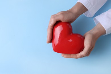 Photo of Doctor holding red heart on light blue background, top view. Space for text