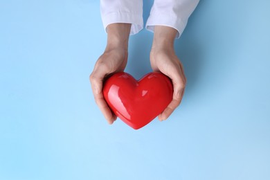 Photo of Doctor holding red heart on light blue background, top view