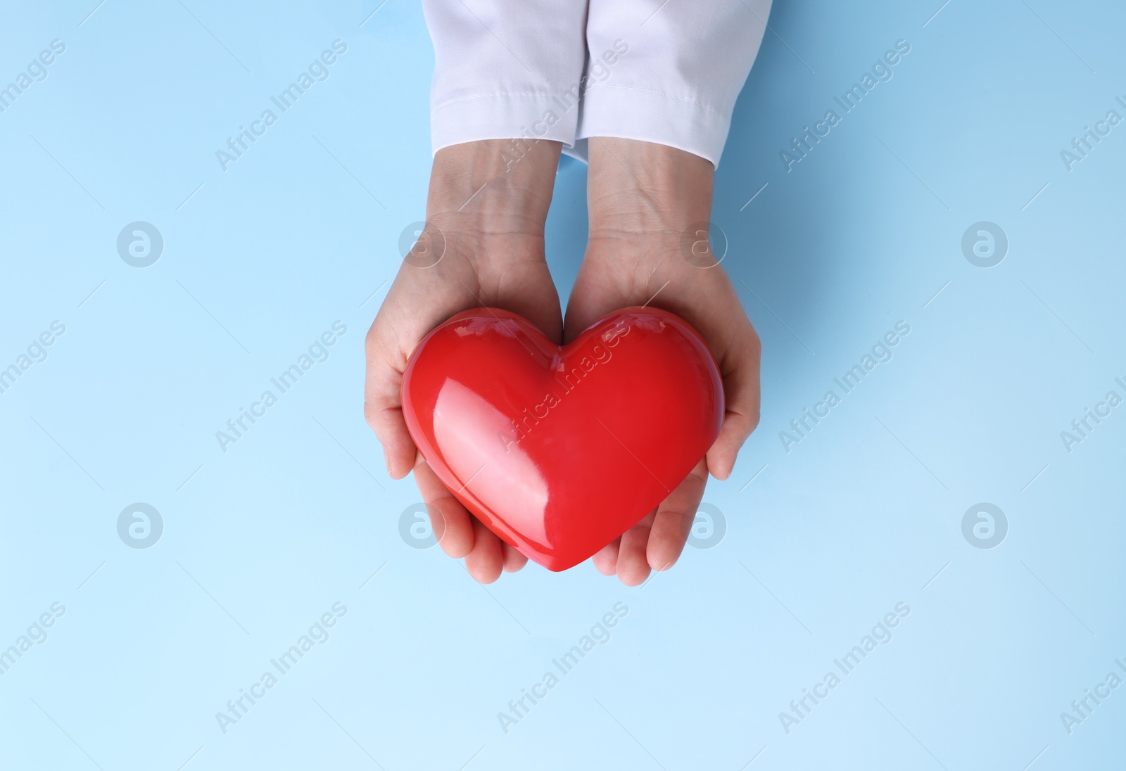 Photo of Doctor holding red heart on light blue background, top view