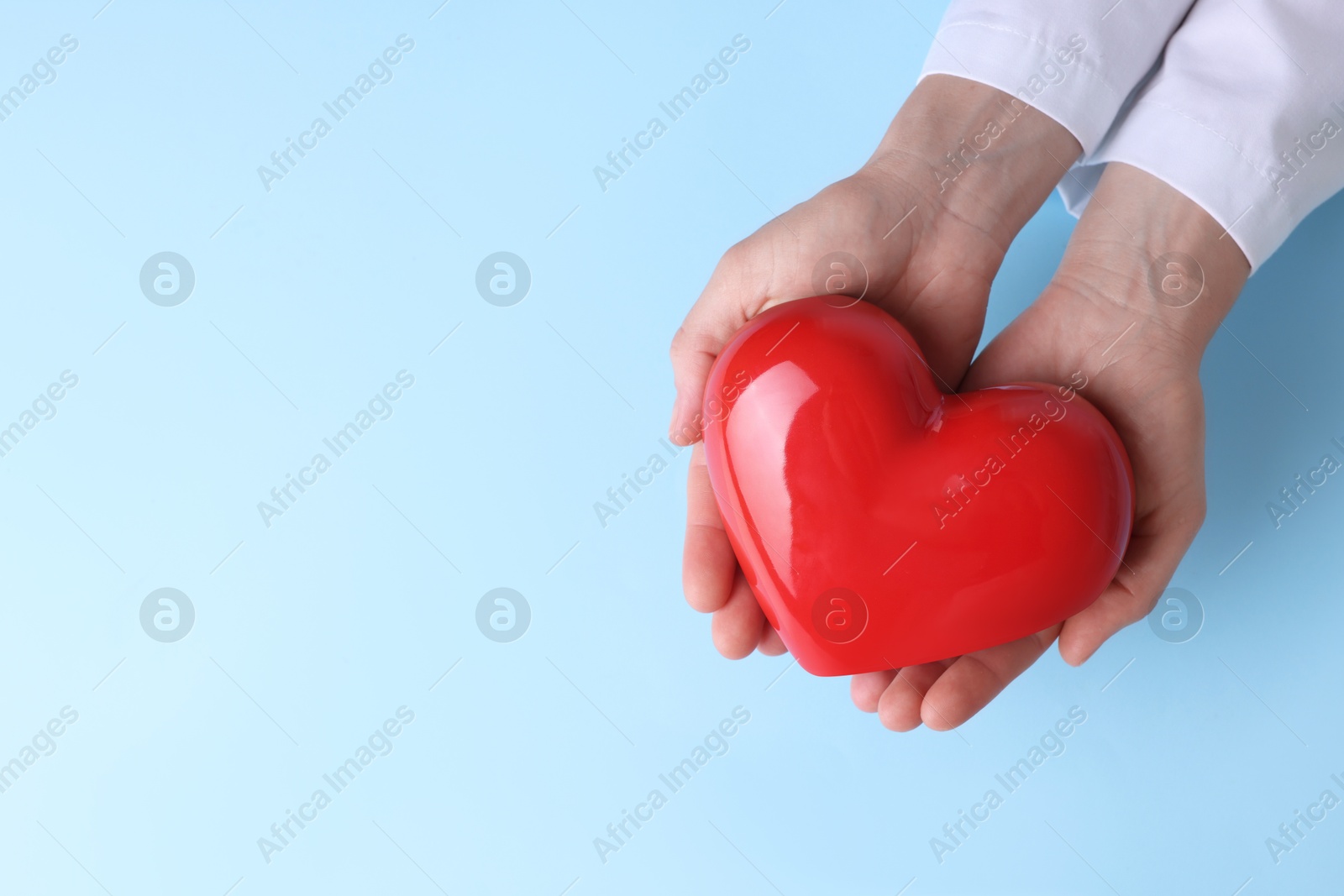 Photo of Doctor holding red heart on light blue background, top view. Space for text