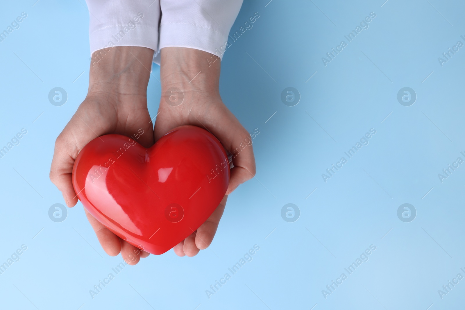 Photo of Doctor holding red heart on light blue background, top view. Space for text