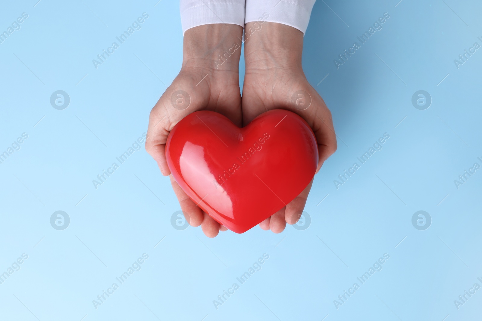 Photo of Doctor holding red heart on light blue background, top view