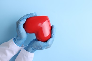 Photo of Doctor holding red heart on light blue background, top view. Space for text