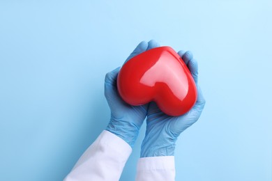 Photo of Doctor holding red heart on light blue background, top view