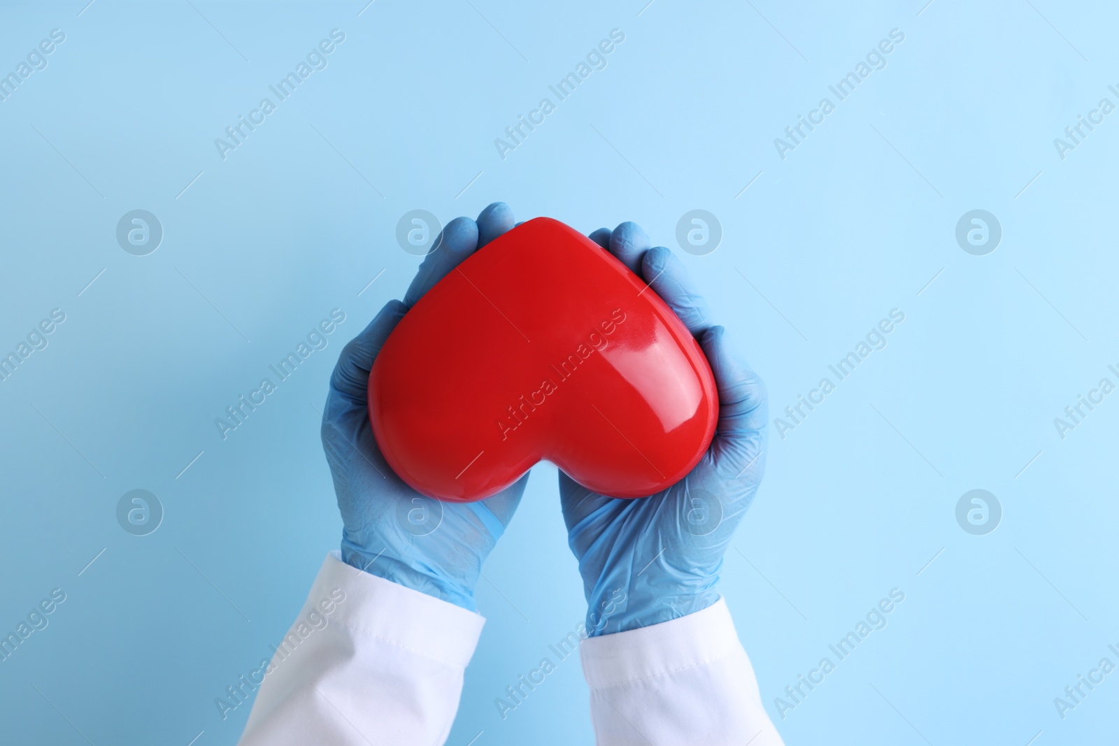 Photo of Doctor holding red heart on light blue background, top view