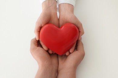 Photo of Doctor and patient holding red heart on white background, top view