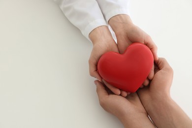 Photo of Doctor and patient holding red heart on white background, top view. Space for text