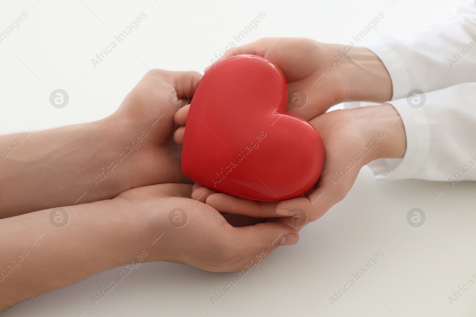 Photo of Doctor and patient holding red heart on white background, closeup