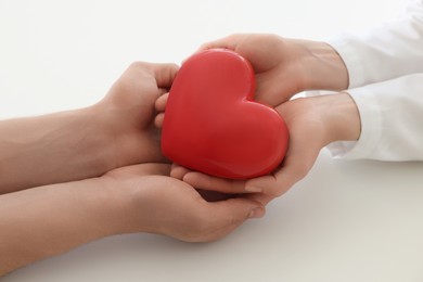 Photo of Doctor and patient holding red heart on white background, closeup
