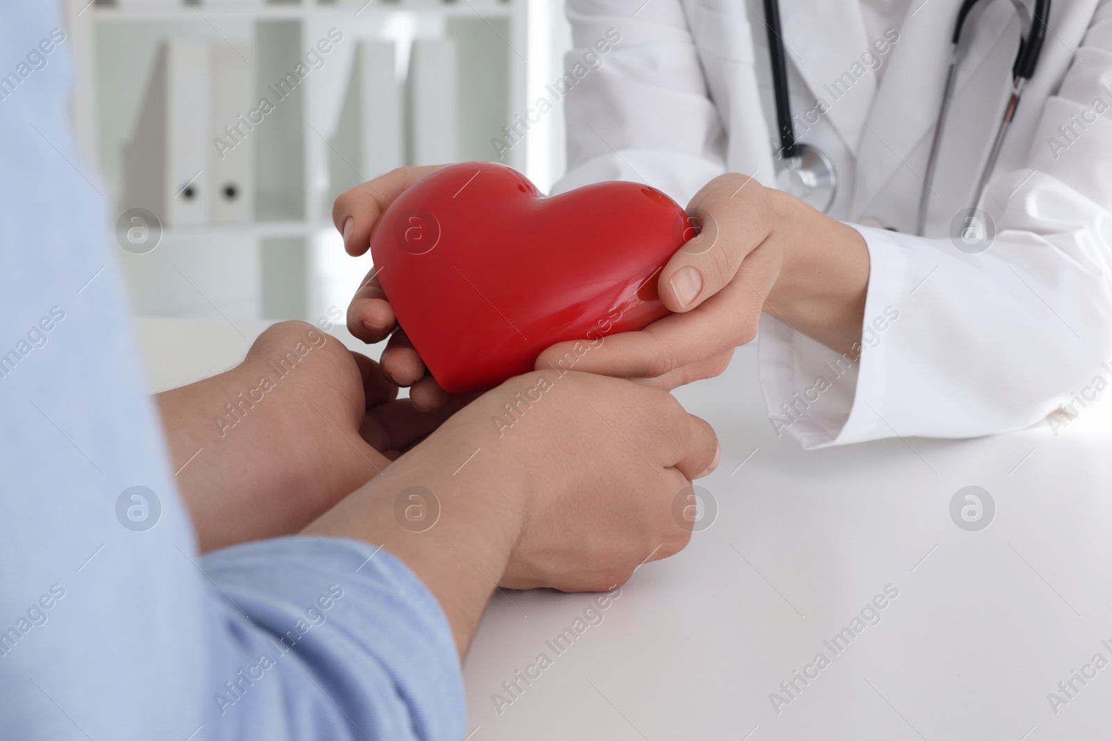 Photo of Doctor giving red heart to patient at white table in clinic, closeup