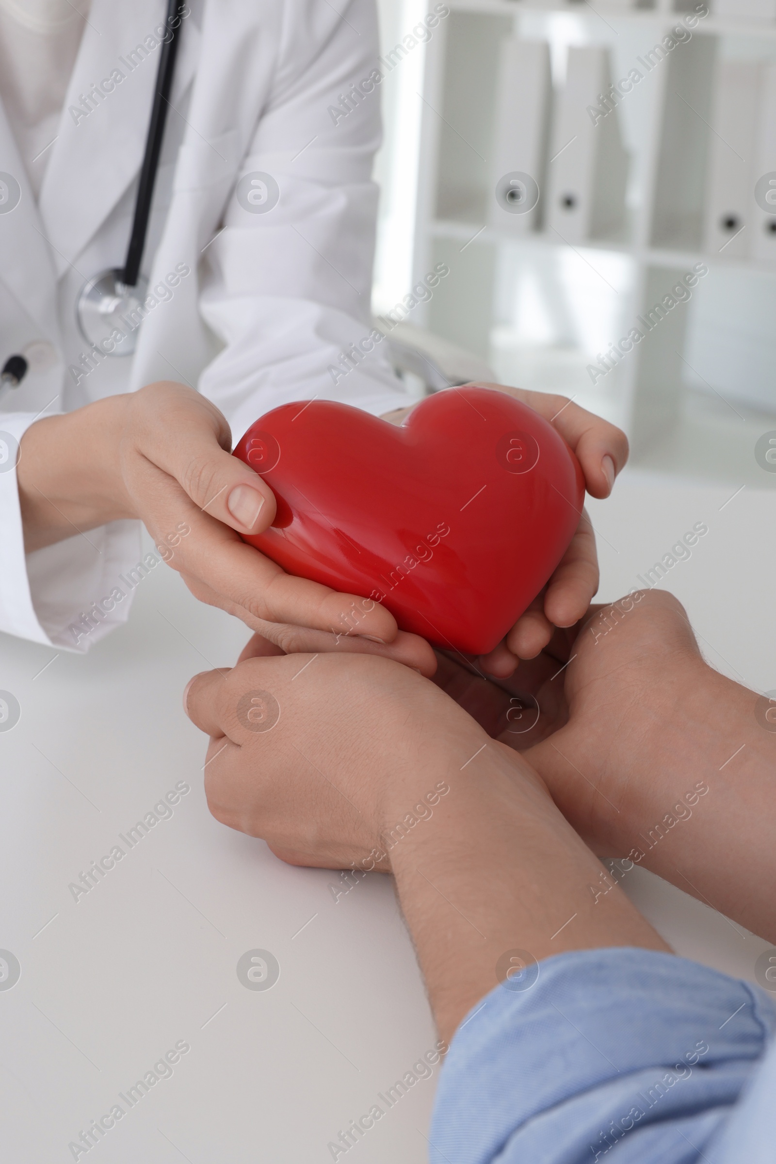 Photo of Doctor giving red heart to patient at white table in clinic, closeup