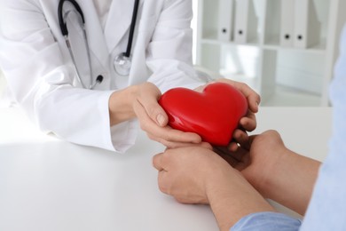 Photo of Doctor giving red heart to patient at white table in clinic, closeup