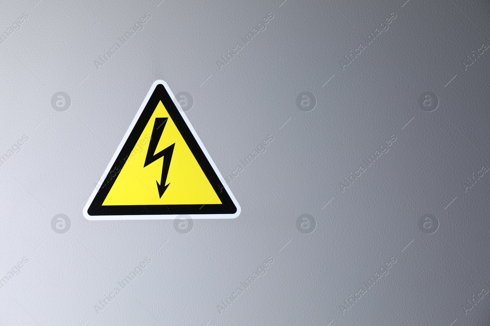 Photo of Yellow danger warning sign on grey wall, space for text. Dangerous voltage