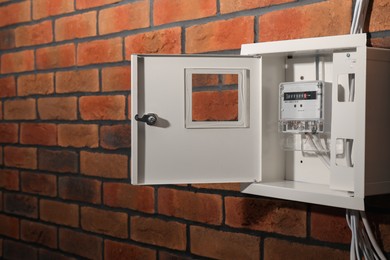 Electric meter in fuse box on red brick wall. Energy measuring device