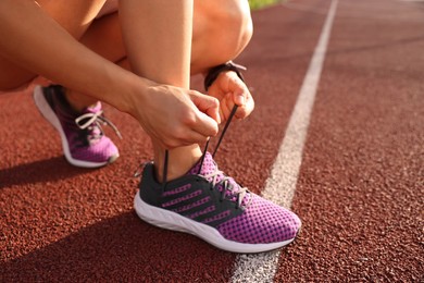 Woman tying shoelace of sneaker at stadium, closeup. Space for text