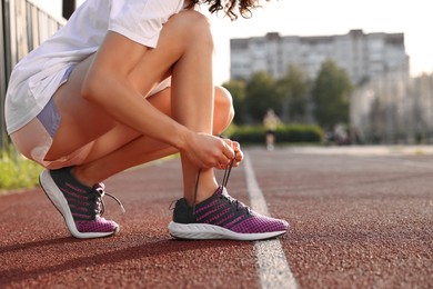 Photo of Woman tying shoelace of sneaker at stadium, closeup. Space for text
