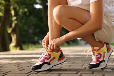 Woman tying shoelace of sneaker outdoors, closeup. Space for text